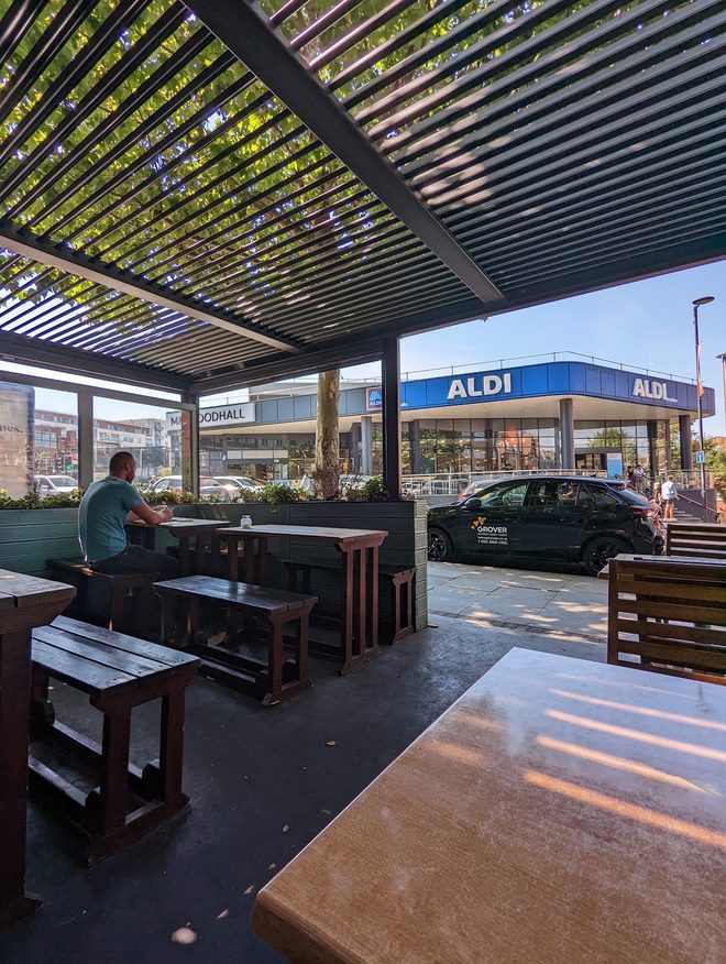 The covered outdoor seating area with its slatted pergola roof and wooden benches