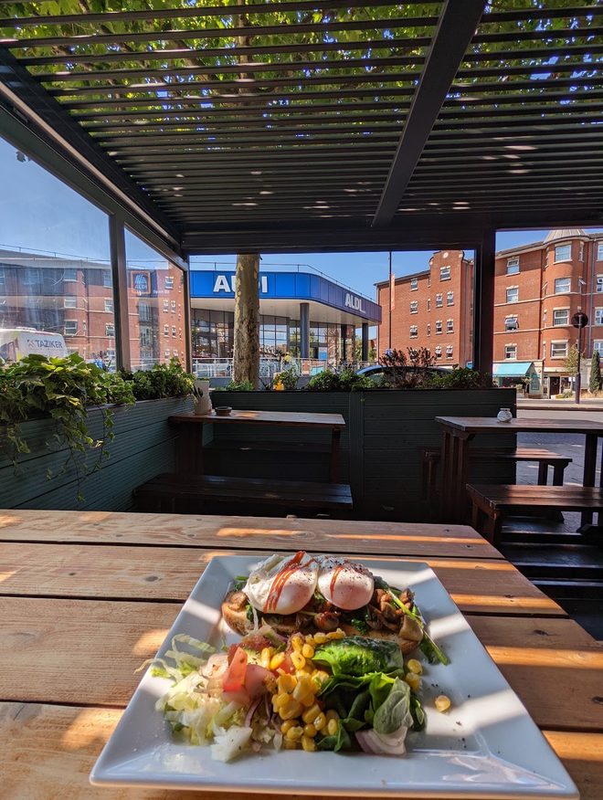 A salad plate on a terrace table with the pergola and planters beyond
