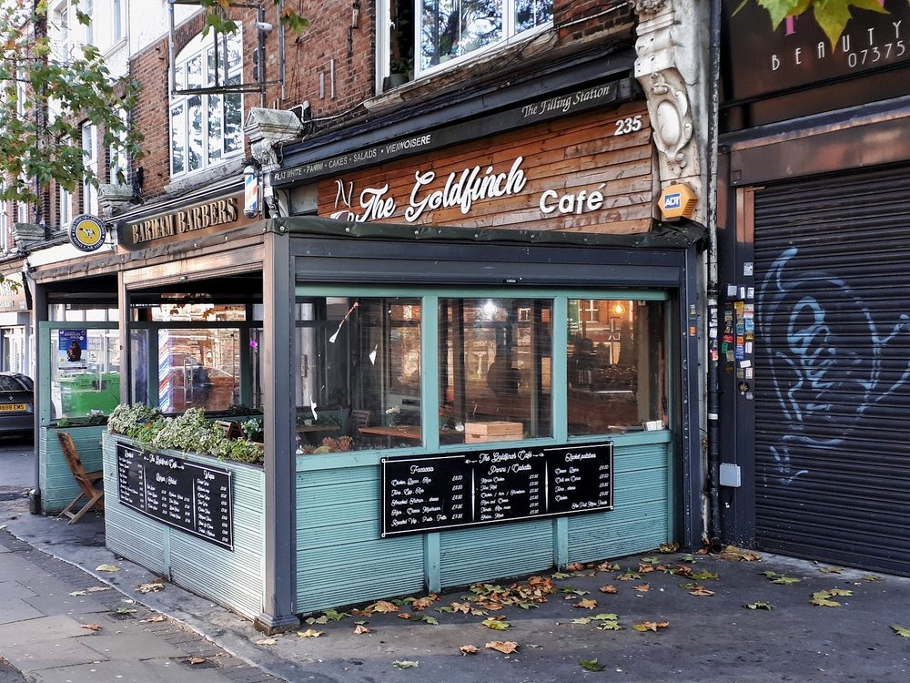 The teal shopfront of The Goldfinch Cafe on Streatham High Road, with window planters and chalkboard menus